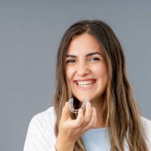 Beautiful smiling Turkish woman is holding an invisalign bracer in a grey background studio with copy space